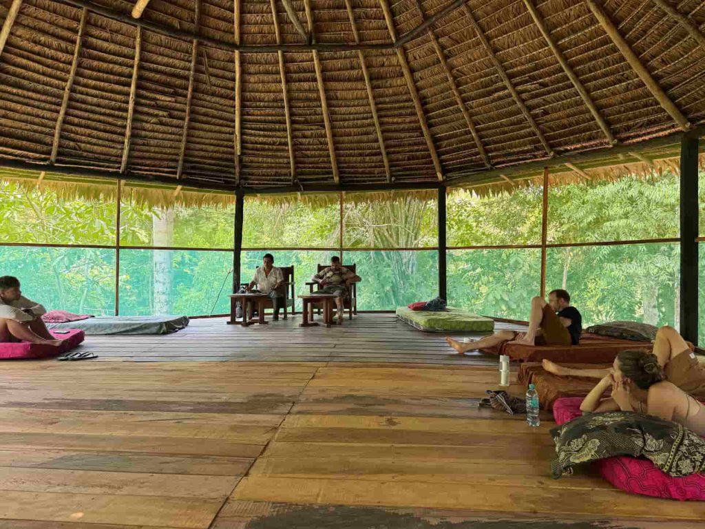  Daytime view inside the maloka temple at La Luna del Amazonas with guests relaxing and the Amazon jungle visible through the screened walls
